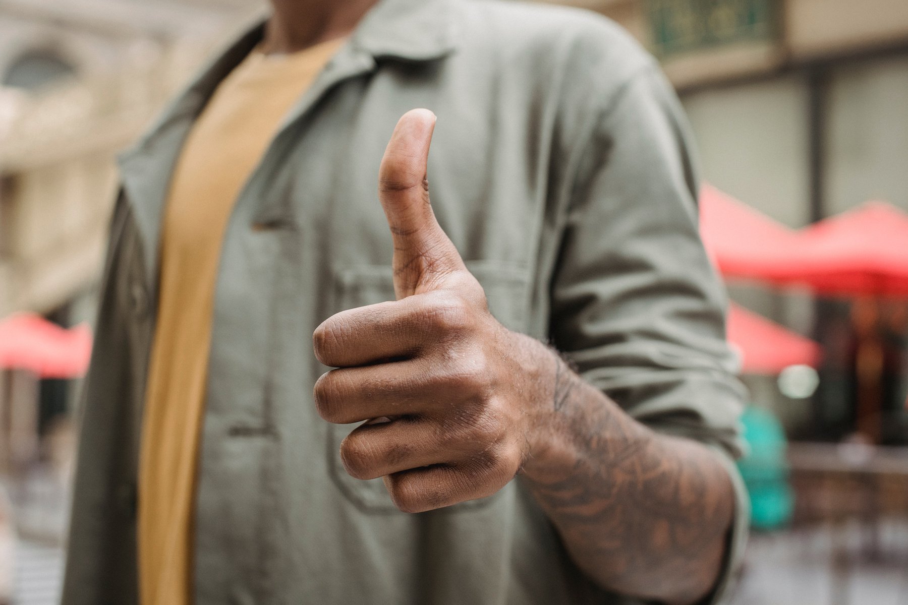 Anonymous ethnic man demonstrating thumb up sign on street