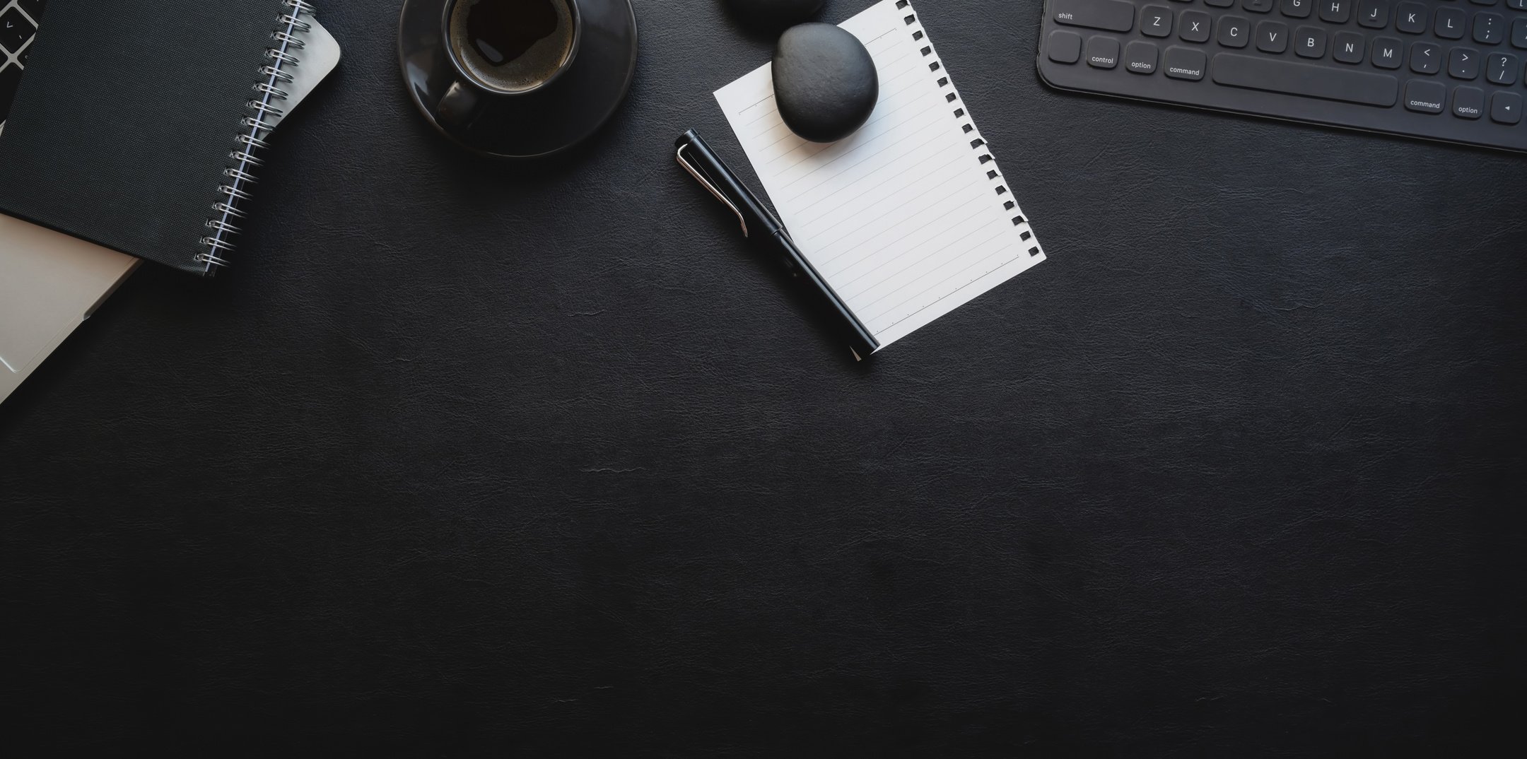 Sheet of paper with pen placed on black table near planner and keyboard